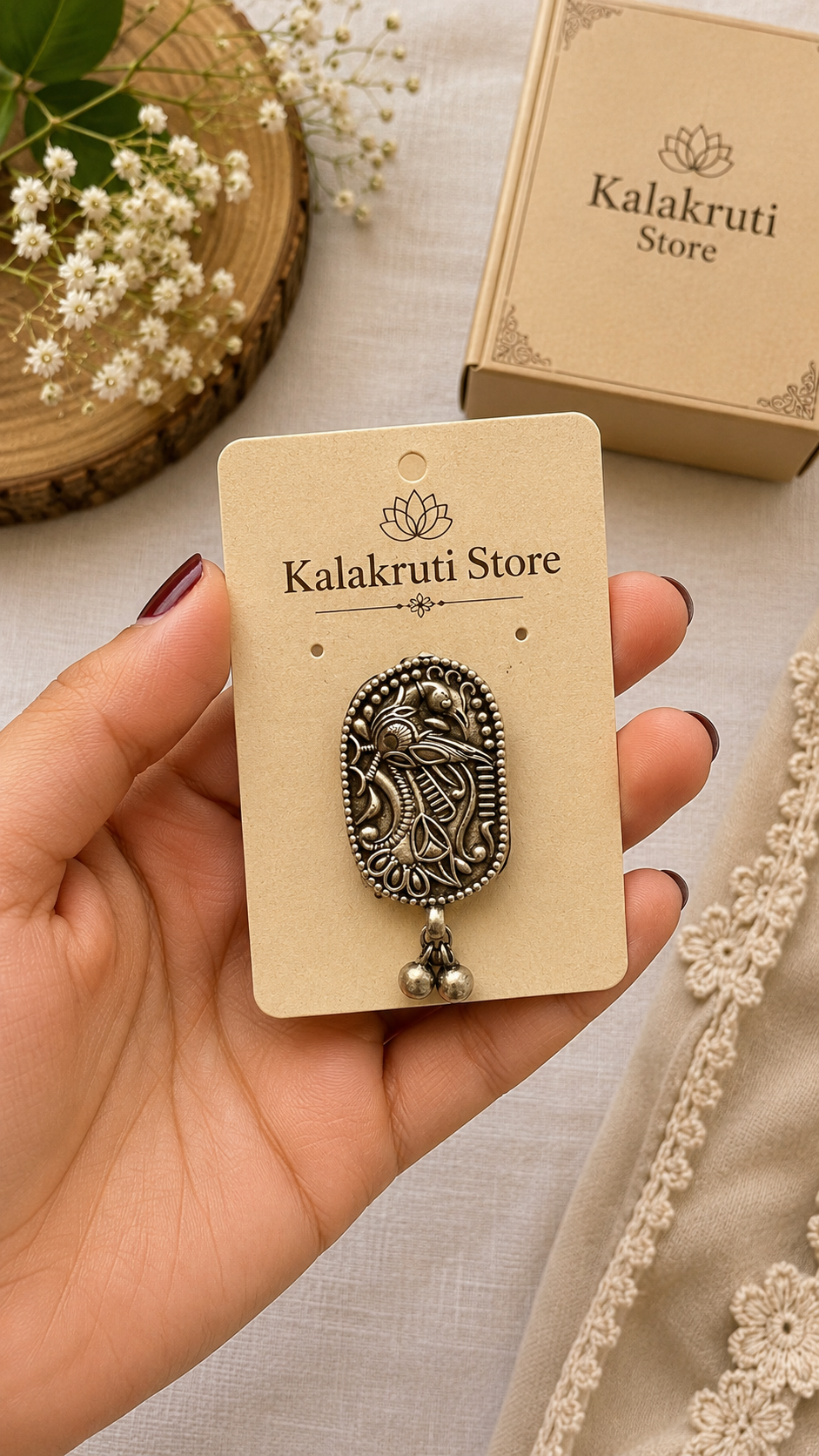 A hand holds a vintage-style oval pendant with an embossed bird design on a beige card from Kalakruti Store. The pendant has an antique silver finish and a small dangling bead.